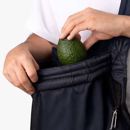 Detalle de una mano guardando un aguacate en el bolsillo lateral del Bolso Cosechador.